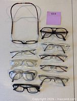 All nine eyeglass frames and one neck strap laid out on table