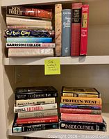 All 23 hardcover fiction books on two shelves with identifying Post-it note