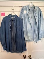 Two denim shirts on hangers, one dark indigo, one light blue with paint stain