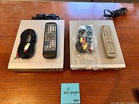 Top view of both DVD players with remotes and cables displayed