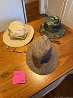 Three hats laid out: beige-edged bucket hat, camo boonie, tweed fedora
