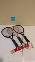 Three racquets overlapped with red wrist strap tether placed below