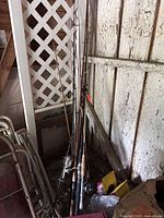 Cluster of six fishing rods leaning against wall with attached reels; visible wear