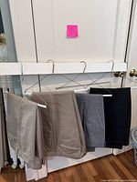 Four pairs of dress pants in khaki, tan, light grey and charcoal/black hanging