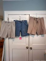 Three pairs of shorts: beige twill, blue denim, tan twill hanging on door