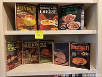 Front view of eight hardcover cookbooks arranged on two shelves