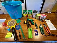 All items laid out on countertop including bucket, fertilizers, insect spray, bug zapper, nozzles, pruners and small tools