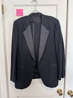 Front view of black tuxedo jacket on hanger showing peak satin lapels and overall style