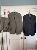 Full view of olive jacket with trousers and charcoal jacket hanging on door