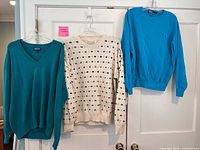 Three sweaters hanging: teal V-neck, cream patterned, bright turquoise crewneck