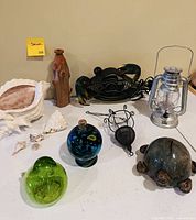 All items arranged on table: ceramic turtle bank, lantern, crab fan, wooden vase, hanging decor, glass pieces, large shell, small shells
