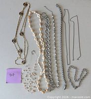 Assorted shell, pearl, gold-tone and silver-tone metal necklaces laid out for full-length view