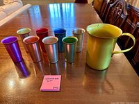 Frontal view of yellow pitcher and eight multicolored tumblers on table
