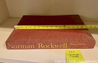 Cover and spine of Norman Rockwell hardcover art book with tape measure for scale