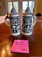 Front view of both German stoneware beer steins showing relief panels and pewter lids
