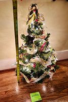 Front view of decorated tabletop tree with lights on and tape measure showing 24-inch height