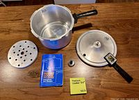 Pot, lid, regulator weight, steamer rack, and manual laid out on table