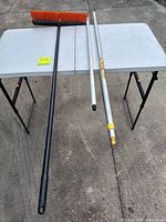 Full view of broom with black pole and two separate silver poles on table