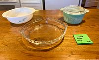 Image shows three primary bakeware pieces: turquoise Butterprint casserole with lid, white blue-wheat mixing bowl, clear glass pie dish