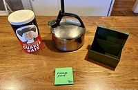 Quaker Oats tin canister, stainless steel kettle, green metal box displayed on wooden surface