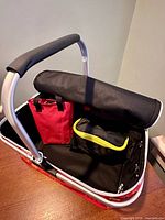 Interior of red insulated basket showing aluminum handle, rolled stool, red bag, black bag