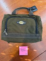 Front view of olive canvas Ricardo toiletry bag showing emblem, zippers and handle
