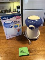 Rival blue and white electric snow cone maker with attached power cord alongside original box