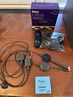 Overall view of Roku Ultra box, Roku remote, Chromecast puck, power adapters, cables on tabletop