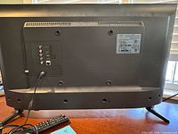 Rear view of Samsung TV showing input ports, stand, attached power cable and remote