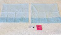 Two light blue satin pillowcases with lace trim laid flat on bedspread
