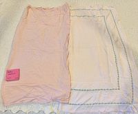 Two baby blankets side-by-side: left solid pink, right white with floral stitched border and scalloped hem