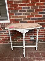 Angled frontal view of distressed white wooden side table on brick floor