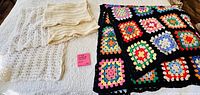 All three afghans laid out: multicolour granny-square, ivory cable-knit, white lace crochet