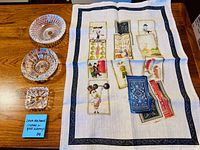 Tea towel spread out next to three clear cut glass dishes showing size, pattern and condition