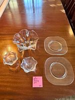 all five clear glass pieces arranged on table: large centerpiece bowl, two small ruffled bowls, two square plates