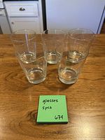 Five clear straight tumblers arranged on wooden surface