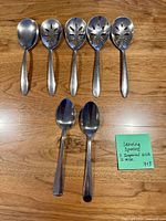Seven stainless steel serving spoons arranged on wood surface, four slotted, three solid