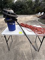 Blue Shop-Vac HangUp vacuum with hose coiled on top, metal wand resting on table, orange extension cord beside