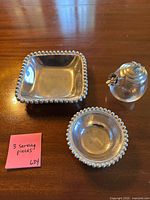 Square and round silver-plated beaded rim bowls, glass jam jar with silver lid displayed on table