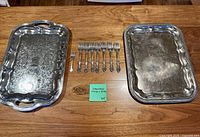 Two ornate stainless steel trays and seven matching forks arranged on wooden surface