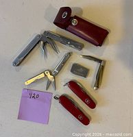 All eight items arranged on tabletop including SwissTool, sheath, knives, mini-tool and stone
