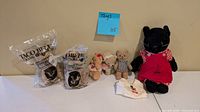 All items in lot on table: two sealed Taco Bell chihuahua plush in bags, one loose chihuahua, three mini teddy bears, black Alli Cat plush, small white T-shirt