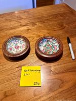 Front view of both circular wood plaques with floral porcelain centres and size reference marker