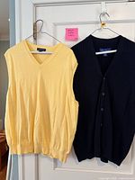 Yellow Lands' End V-neck sweater vest and navy Alan Flusser button-front vest hanging on door