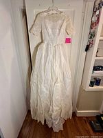 Full view of vintage ivory/cream ball gown wedding dress hanging on door showing full skirt and short sleeves