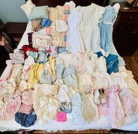 All garments spread on bed showing variety of dresses, onesies, tops, accessories, shoes and blanket
