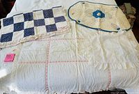 All four quilts laid on bed: blue/white checkerboard, cream with blue border, white with pink sashing, white ruffled cover