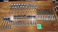 All 51 pieces of Wallace flatware laid out in groups by type on wooden surface