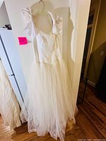 Full front view of white satin bodice and tulle skirt ball gown on hanger