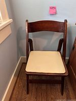 Front view of wood folding chair showing beige padded seat and brown wooden frame